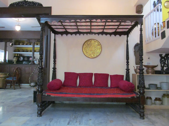 An intricately carved four post antique cot with canopy can be re-purposed as a divan with arrangement of bolsters and pillows